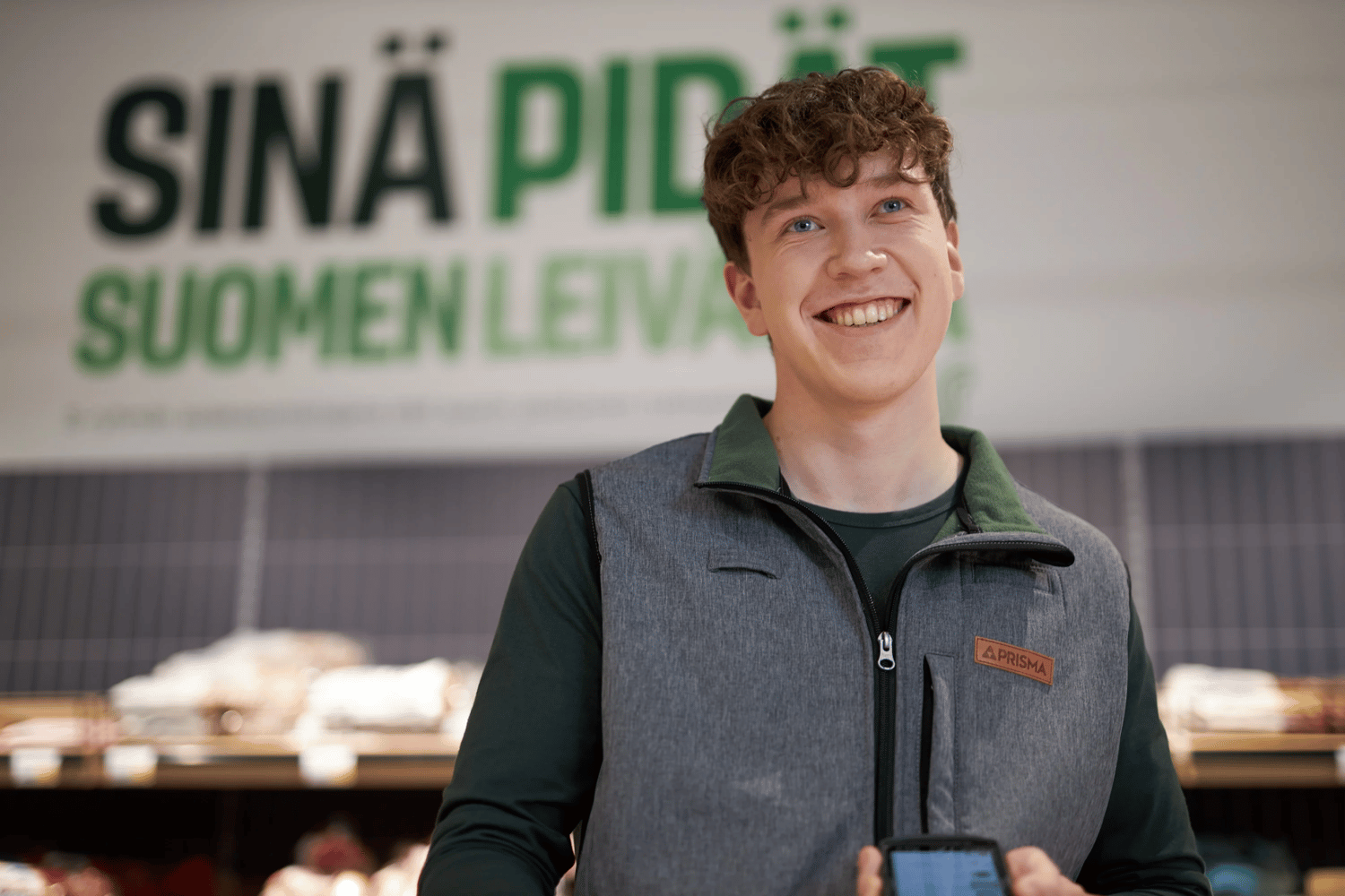 An S Group employee smiling at the camera in front of a bread isle